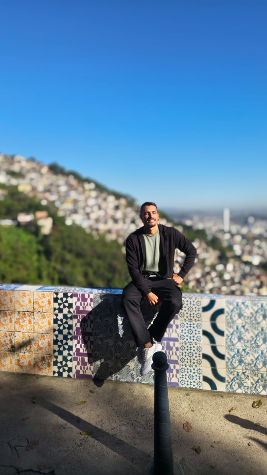 Turista sentado em muro de azulejos com vista da favela ao fundo