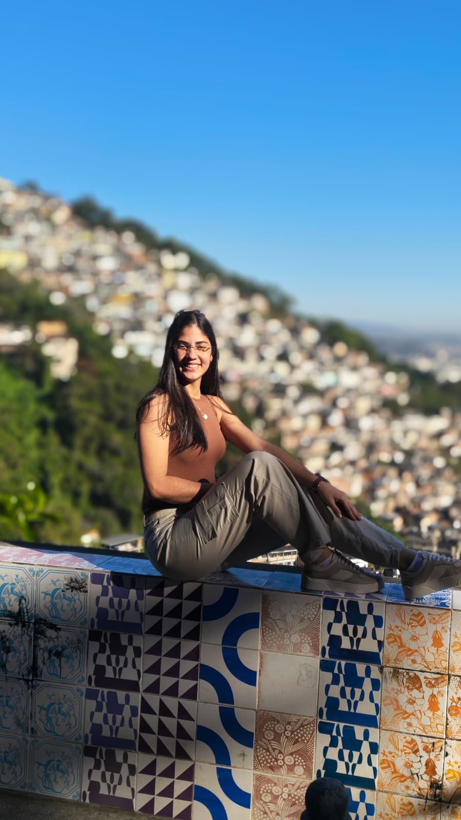 Turista sentada em muro de azulejos com vista da favela ao fundo