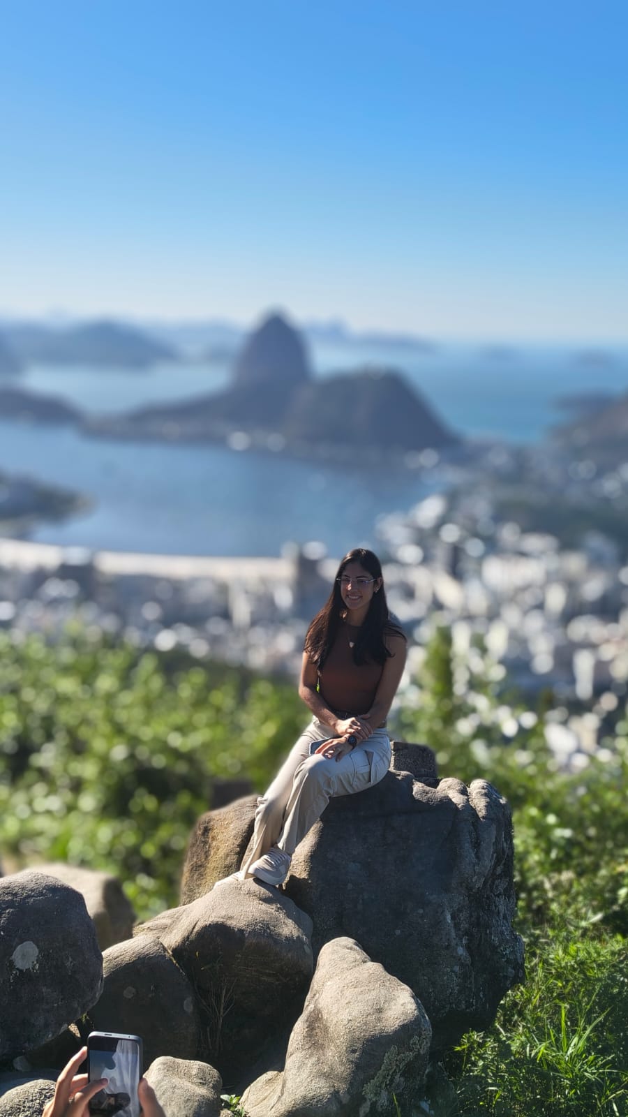 Turista sentada em pedras de mirante com o Pão de Açúcar ao fundo