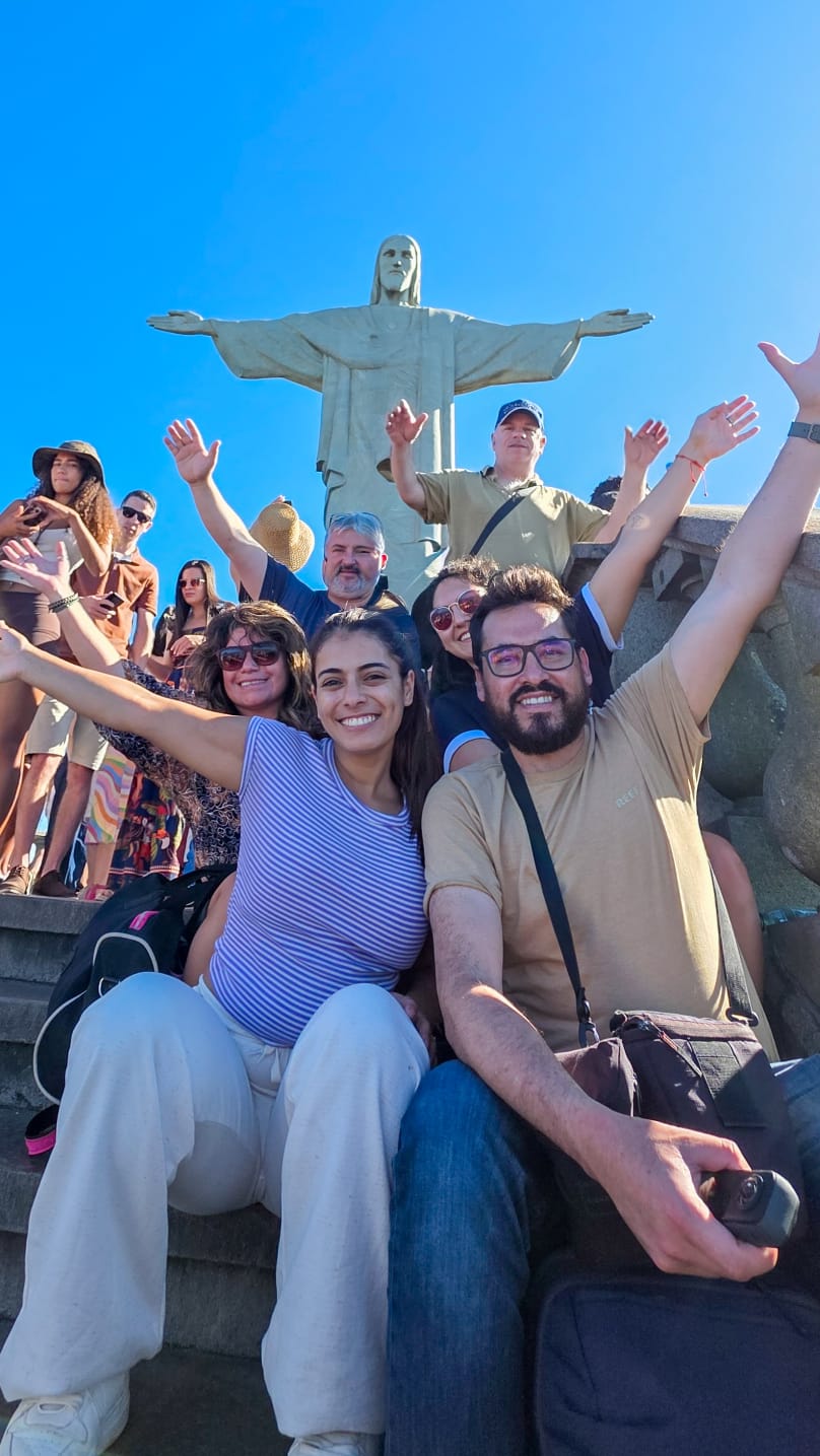 Grupo de turistas sorrindo aos pés do Cristo Redentor