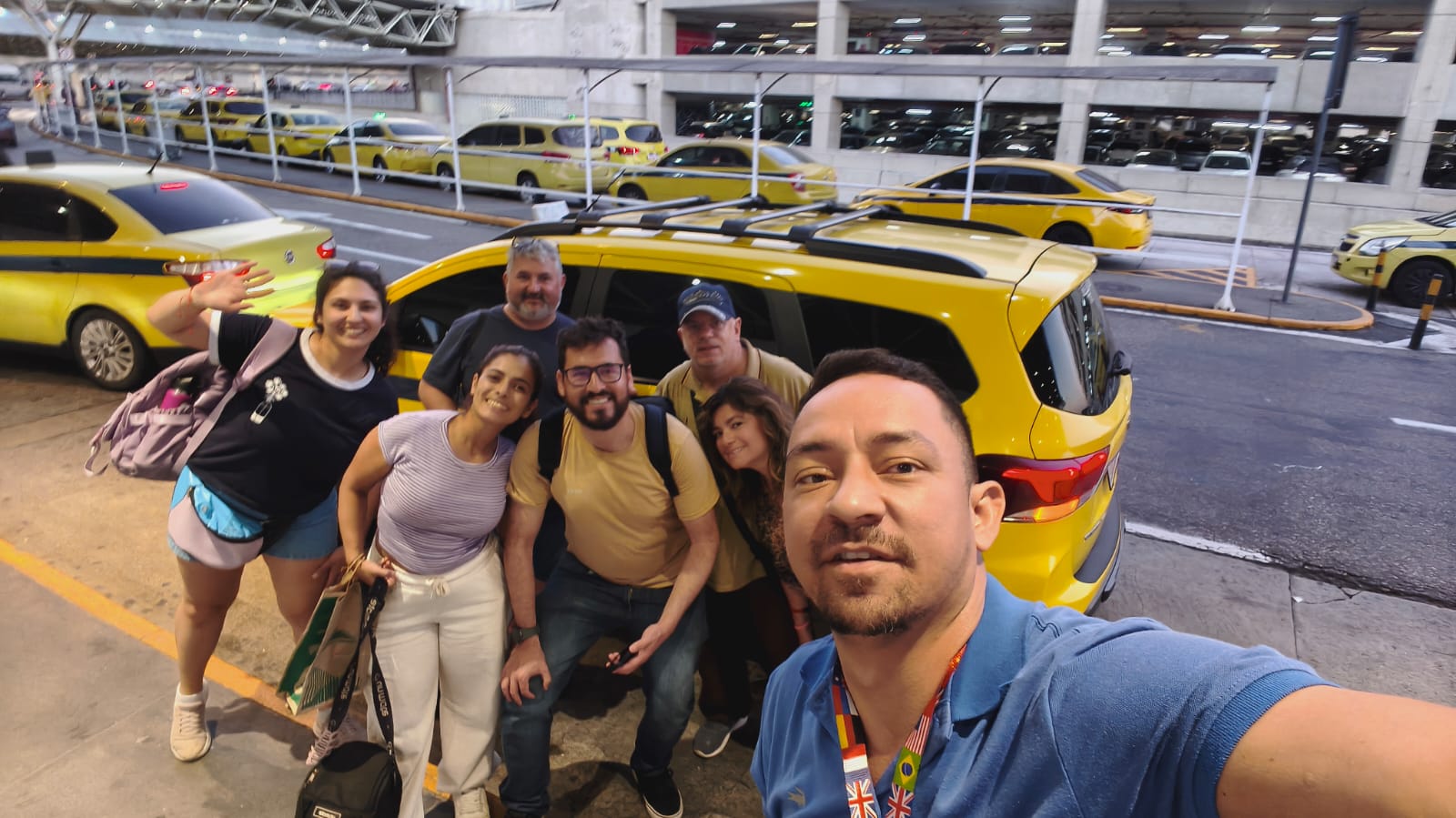 Grupo de turistas sorrindo ao lado dos táxis amarelos no aeroporto